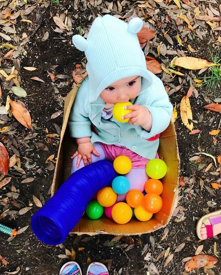 A baby sits in a cardboard box full of balls