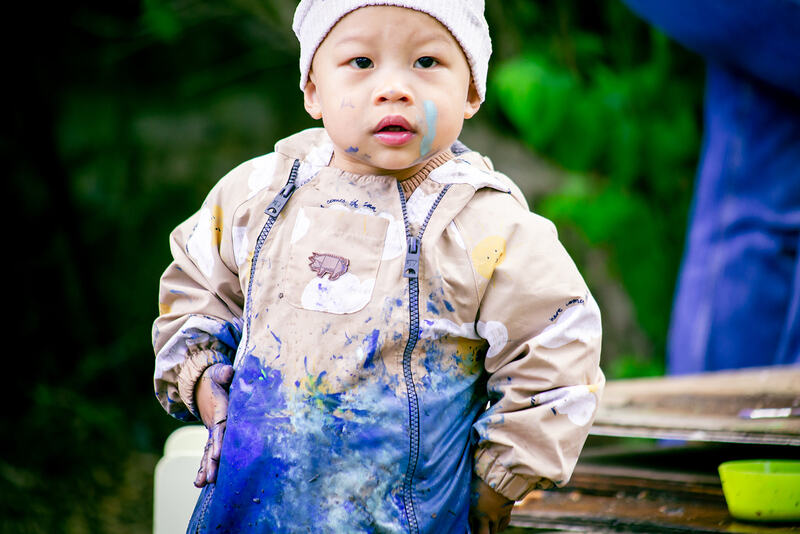 A toddler wearing a rainsuit splattered with blue paint