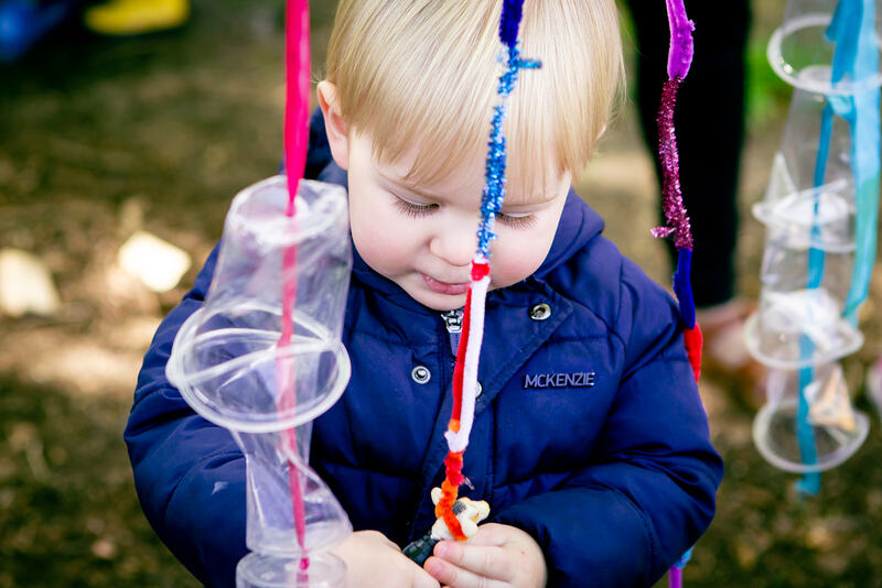 A toddler plays with hanging plastic cups and pipe cleaners.