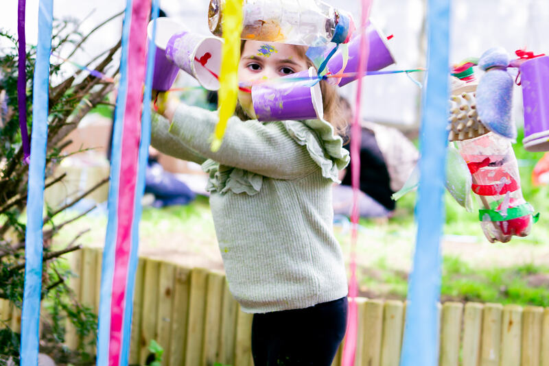 A child plays with a curtain of blue and pink ribbons and strings of dangling purple paper cups. 