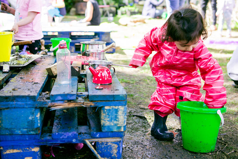 A child picks up a green bucket next to a  mud kitchen.