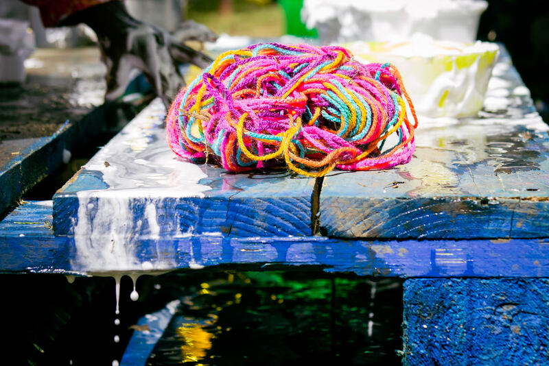 A loose ball of rainbow coloured wool sits on a blue wooden pallet. Watery white shaving foam drips off the edge.