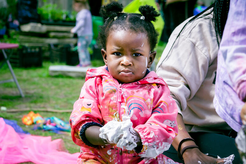 A baby frowns at the camera, her hands covered in shaving foam.