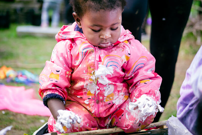 A baby looks down at her hands, which are covered in shaving foam.