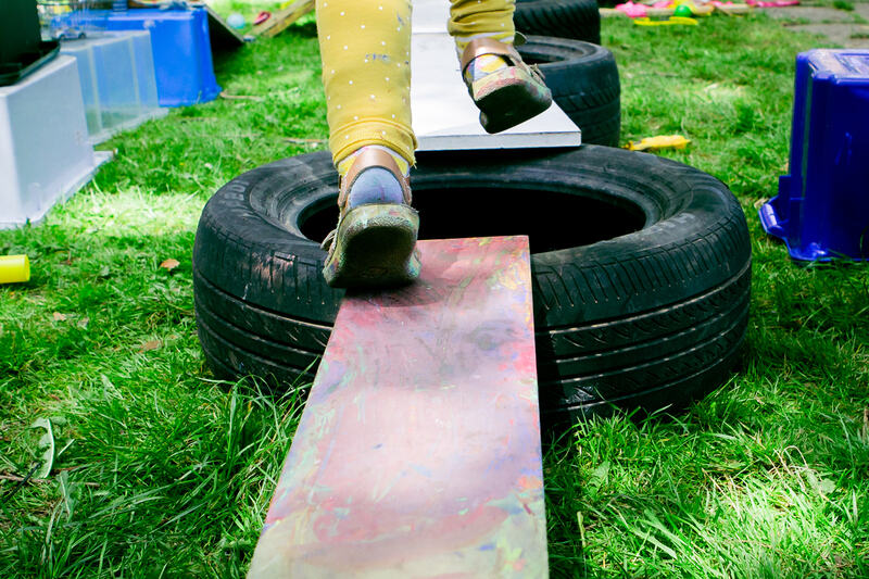 A child's feet jump across wooden planks balanced on a tyre.