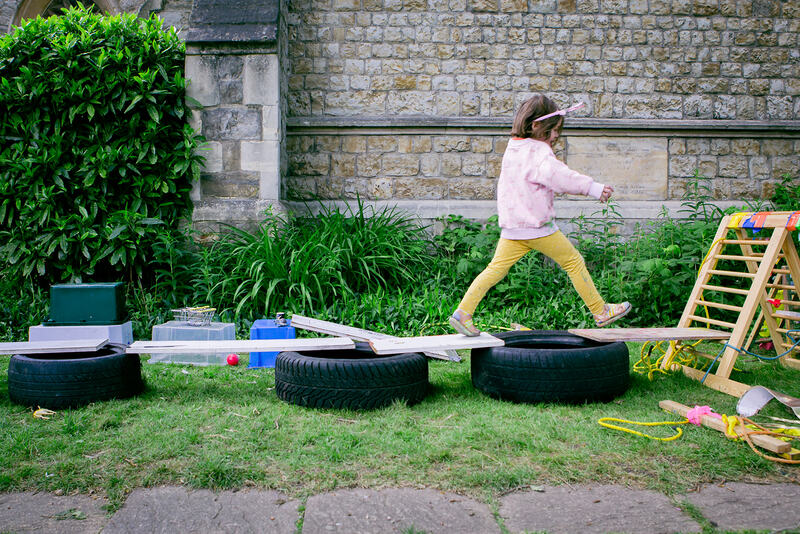 A child walks along a series of bridges made from pieces of shelving balanced on tyres.