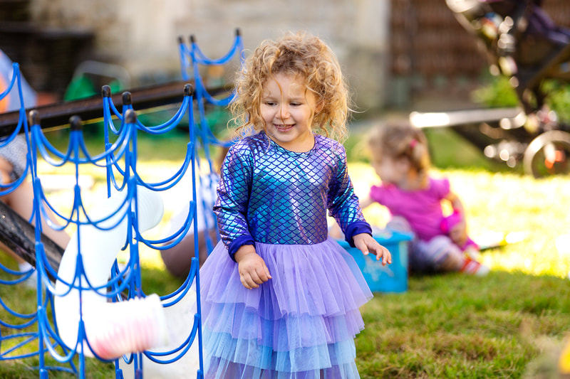 A child wearing a shimmering purple tutu dress smiles next to some water stands.