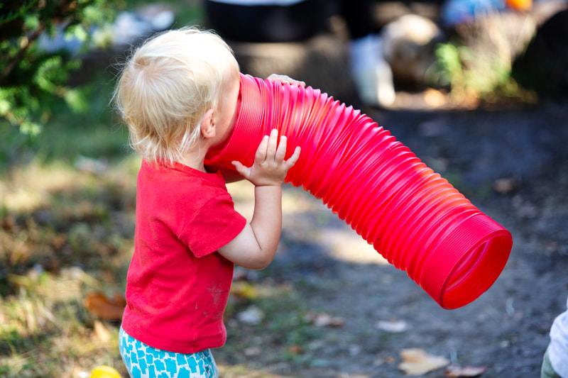 A child holds up to their face a large red plastic bendy tube.