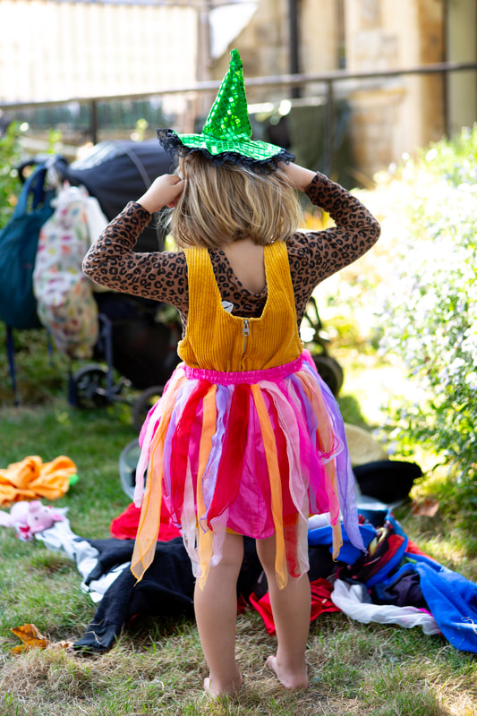 A child wearing a colourful tutu puts a little green witch hat on their head.