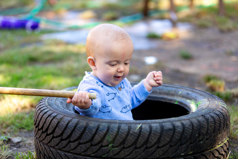 A young baby sits inside a tyre, holding a stick.